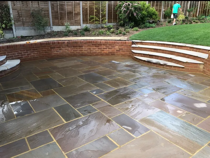 Curved brick retaining wall with wide stone steps up to a lawn, above a sandstone patio